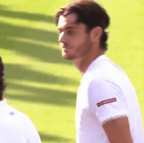 A Man Wearing A Chipotle Shirt Stands On A Lush Green Field GIF