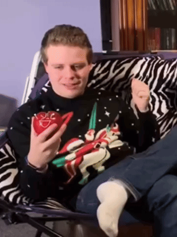 A Man Wearing A Christmas Sweater Holds A Red Heart GIF