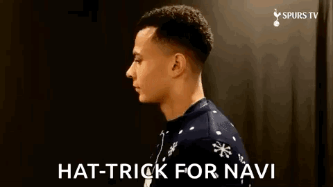 A Man Wearing A Christmas Sweater Is Standing In Front Of A Black Wall And Says `` Hat Trick For Navi '' . GIF