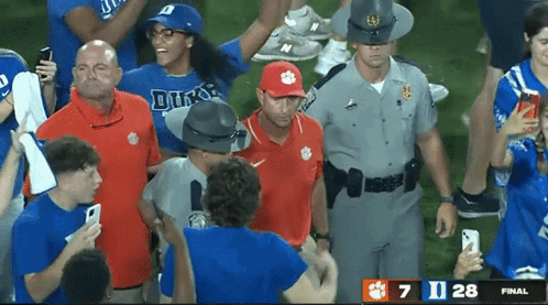 a man wearing a clemson hat is surrounded by fans and police officers