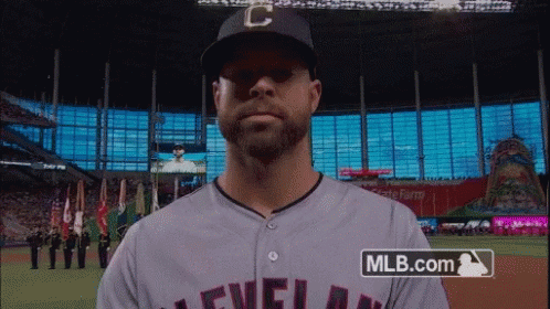 A Man Wearing A Cleveland Baseball Jersey Stands In Front Of A Mlb.com Logo GIF