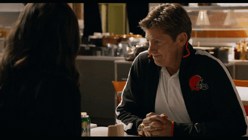 A Man Wearing A Cleveland Browns Jacket Is Talking To A Woman GIF