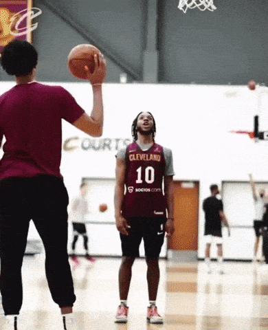 A Man Wearing A Cleveland Jersey Is Throwing A Basketball To Another Man GIF