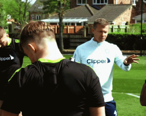 a man wearing a clipper shirt talks to a group of players