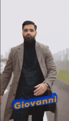 A Man Wearing A Coat And A Black Turtleneck Has The Name Giovanni Written On A Blue Sign GIF