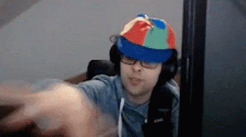 A Man Wearing A Colorful Hat And Headphones Is Sitting In Front Of A Computer Monitor . GIF
