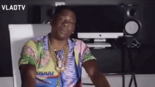 A Man Wearing A Colorful Shirt And A Gold Chain Is Sitting In Front Of A Computer . GIF