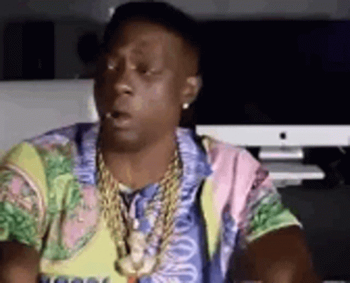 A Man Wearing A Colorful Shirt And A Necklace Is Sitting In Front Of A Computer . GIF