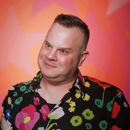A Man Wearing A Colorful Shirt With Flowers On It Looks At The Camera GIF