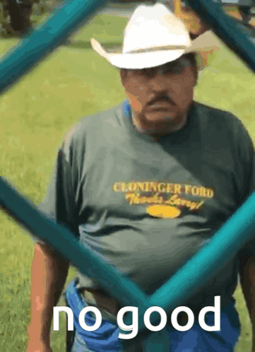 A Man Wearing A Cowboy Hat And A Cloninger Ford Shirt Stands In The Grass GIF