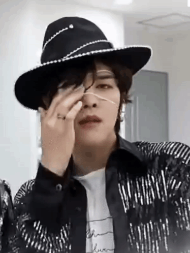 A Man Wearing A Cowboy Hat And A Jacket Is Covering His Nose With His Hand . GIF