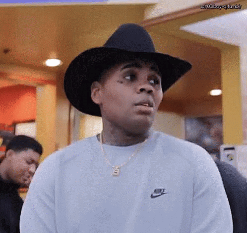 A Man Wearing A Cowboy Hat And A Nike Sweater Is Making A Funny Face . GIF