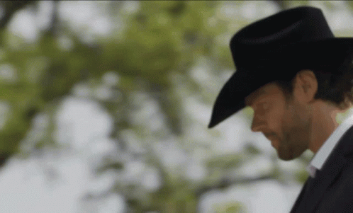 A Man Wearing A Cowboy Hat And A Suit Is Looking Down GIF