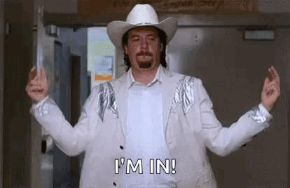 A Man Wearing A Cowboy Hat And A White Suit Is Standing In A Doorway With His Arms Outstretched . GIF