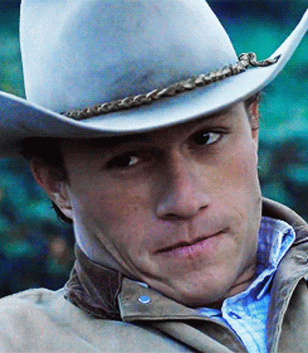 A Man Wearing A Cowboy Hat And Jacket Looks At The Camera GIF