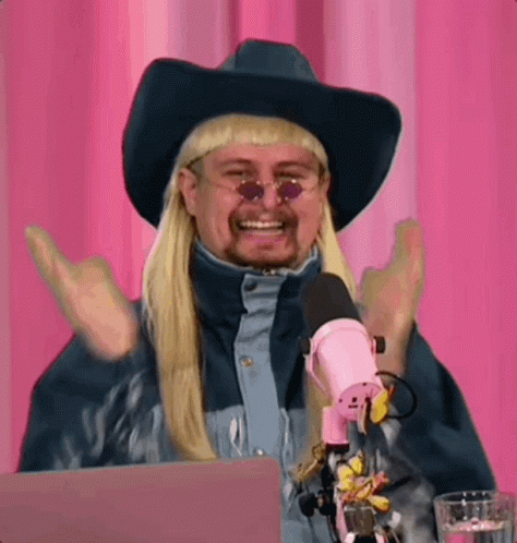 A Man Wearing A Cowboy Hat And Sunglasses Is Sitting In Front Of A Microphone . GIF