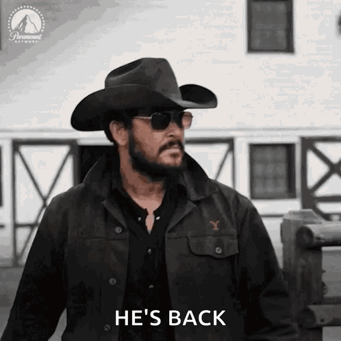A Man Wearing A Cowboy Hat And Sunglasses Is Standing In Front Of A Building And Saying `` He 'S Back '' . GIF