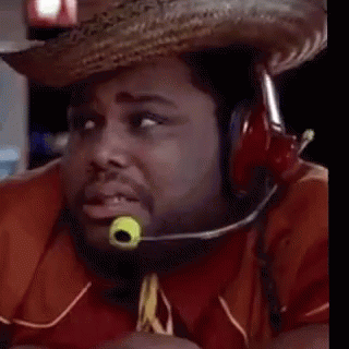 A Man Wearing A Cowboy Hat And Tie With A Green Object In His Mouth Is Looking At The Camera . GIF
