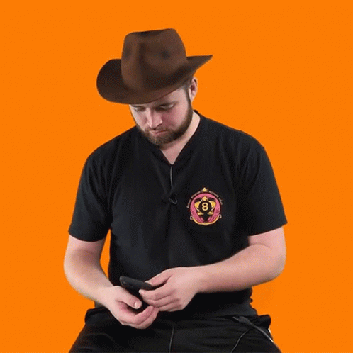 A Man Wearing A Cowboy Hat Is Looking At His Phone And The Word Whoa Is Below Him GIF
