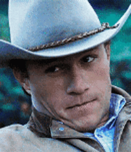 A Man Wearing A Cowboy Hat Is Looking At The Camera . GIF