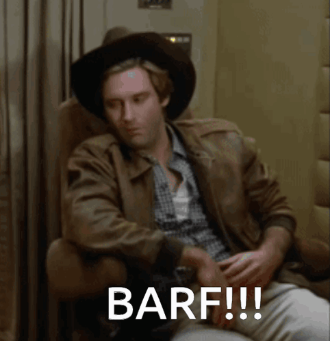 A Man Wearing A Cowboy Hat Is Sitting In A Chair With The Words Barf Written On The Screen GIF