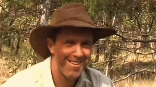 A Man Wearing A Cowboy Hat Is Smiling In Front Of Trees GIF