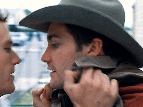 A Man Wearing A Cowboy Hat Is Touching The Face Of Another Man GIF