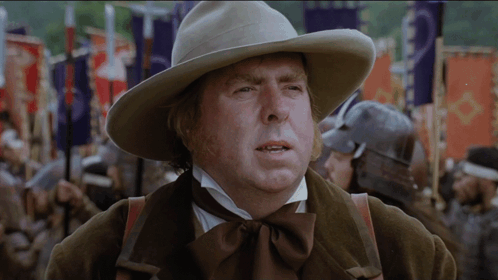 A Man Wearing A Cowboy Hat Stands In Front Of A Crowd Of People GIF