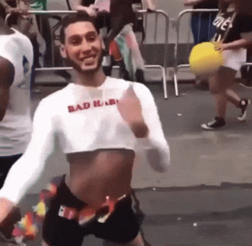 A Man Wearing A Crop Top And Shorts Is Dancing In A Crowd . GIF