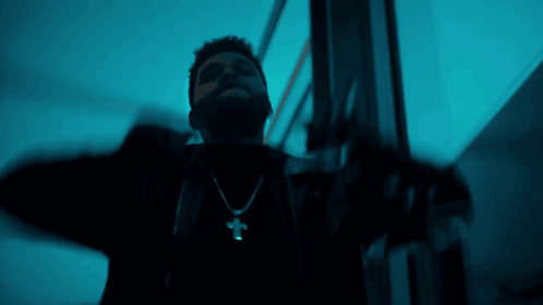 A Man Wearing A Cross Necklace Is Standing In A Dark Room GIF