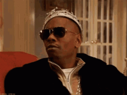a man wearing a crown and sunglasses is sitting on a chair .