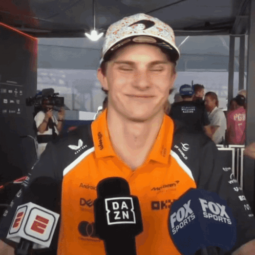 A Man Wearing A Da Zn Shirt Is Talking Into A Microphone GIF
