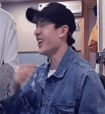 A Man Wearing A Denim Jacket And A Baseball Cap Is Smiling And Laughing . GIF