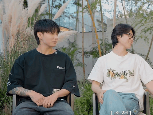 A Man Wearing A Dior Tear T-Shirt Sits Next To A Man Wearing A Black Shirt GIF
