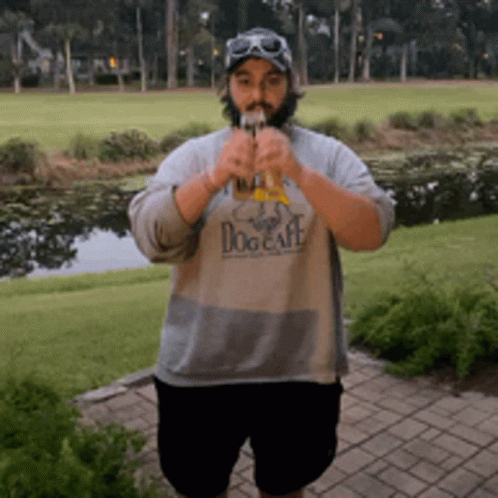 a man wearing a dog cafe shirt is standing in front of a golf course