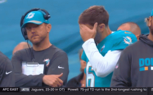 A Man Wearing A Dolphins Jersey Is Covering His Face GIF