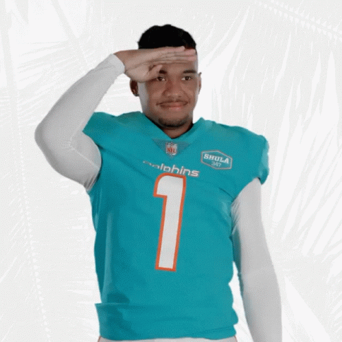 A Man Wearing A Dolphins Jersey Salutes In Front Of A White Background GIF