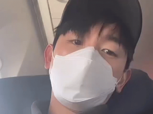 A Man Wearing A Face Mask And A Baseball Cap Is Sitting On A Plane . GIF
