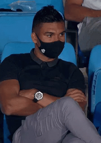 a man wearing a face mask and a watch is sitting in a stadium .