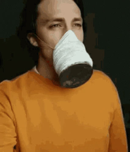 A Man Wearing A Face Mask And An Orange Sweater Is Taking A Selfie . GIF