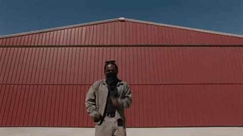 A Man Wearing A Face Mask Is Dancing In Front Of A Red Building GIF