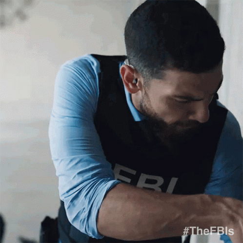 A Man Wearing A Fbi Vest Looks Down At Something GIF