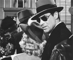 A Man Wearing A Fedora And Sunglasses Is Standing Next To A Woman GIF