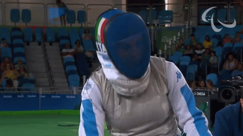 A Man Wearing A Fencing Mask Is Standing In Front Of A Camera That Says Omega GIF