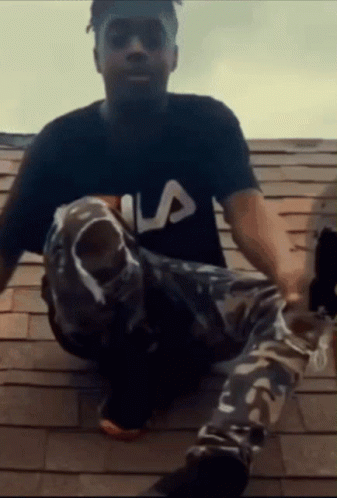 A Man Wearing A Fila Shirt Sits On A Rooftop GIF
