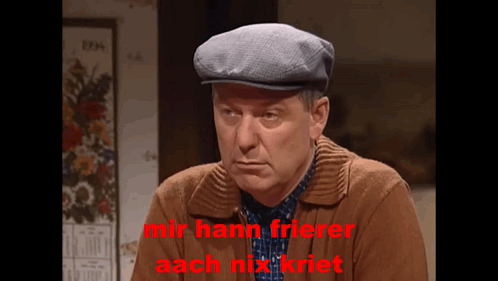 A Man Wearing A Flat Cap And A Brown Jacket Says Mir Hann Frierer Aach Mix Riet GIF