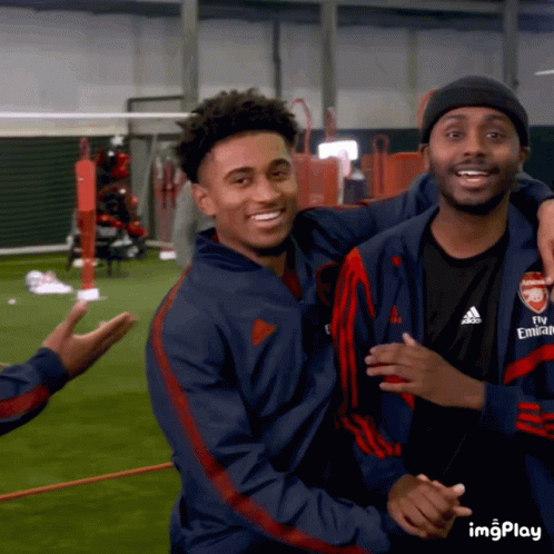 A Man Wearing A Fly Emirates Jacket Hugs Another Man On A Field GIF