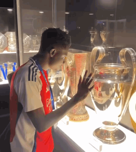 A Man Wearing A Fly Emirates Shirt Touches A Trophy In A Glass Case GIF