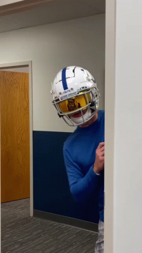 a man wearing a football helmet and goggles is standing in a hallway .