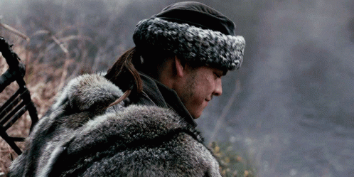 A Man Wearing A Fur Coat And A Hat Is Standing In A Field . GIF
